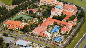 Vista aérea de un complejo turístico con varias edificaciones, una piscina y una cancha de tenis.