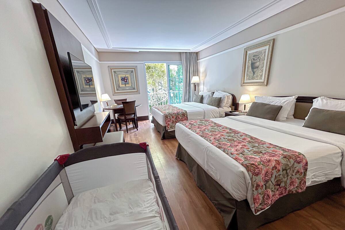 Une chambre d’hôtel avec deux lits, un bureau et une chaise. Il y a deux tables de chevet avec des lampes.