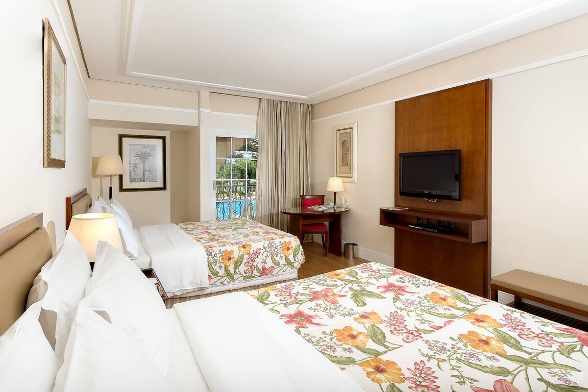 Une chambre d’hôtel avec deux lits, un bureau, une chaise, une télévision et un balcon avec vue.