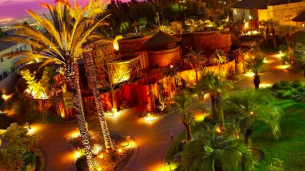 Un resort con edificios de techo de paja, palmeras y un camino bien iluminado.