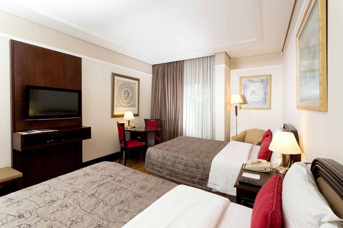 Une chambre d’hôtel équipée d’une télévision, d’un bureau avec une lampe, de deux lits et de tableaux encadrés aux murs.
