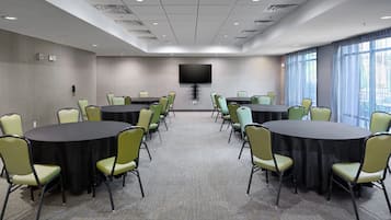 Une salle de conférence équipée de deux tables rondes, de chaises vertes, d’un téléviseur à écran plat et de grandes fenêtres.