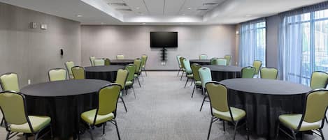 A conference room with two round tables, green chairs, a flat-screen TV, and large windows.