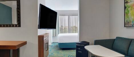 Habitación de hotel con cama, televisión, escritorio, sofá y ventana con cortinas.