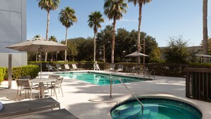 A swimming pool with lounge chairs and umbrellas, surrounded by palm trees and a clear sky. - SpringHill Suites by Marriott Jacksonville (Jacksonville)
