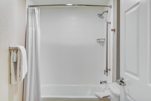 Un baño blanco con cabina de ducha de vidrio, inodoro y perchero.