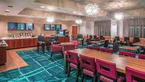 Un espace de restauration d’hôtel comprenant plusieurs tables et chaises, un coin café et un bar.