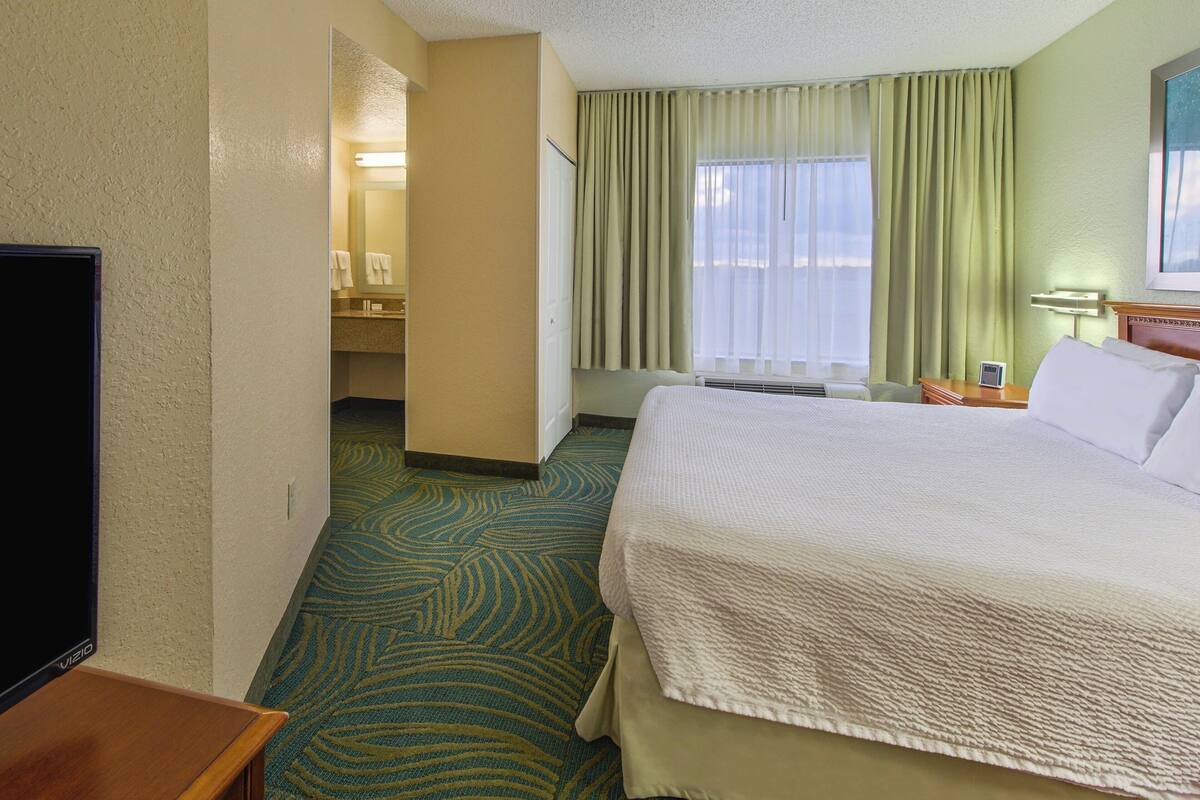 Hotelkamer met een groot bed, een televisie, een badkamer met spiegel en een raam met gordijnen.