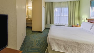 Una habitación de hotel con una cama grande, televisión, baño con espejo y ventana con cortinas.