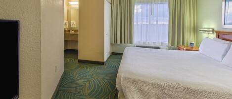 A hotel room with a large bed, a television, a bathroom with a mirror, and a window with curtains.