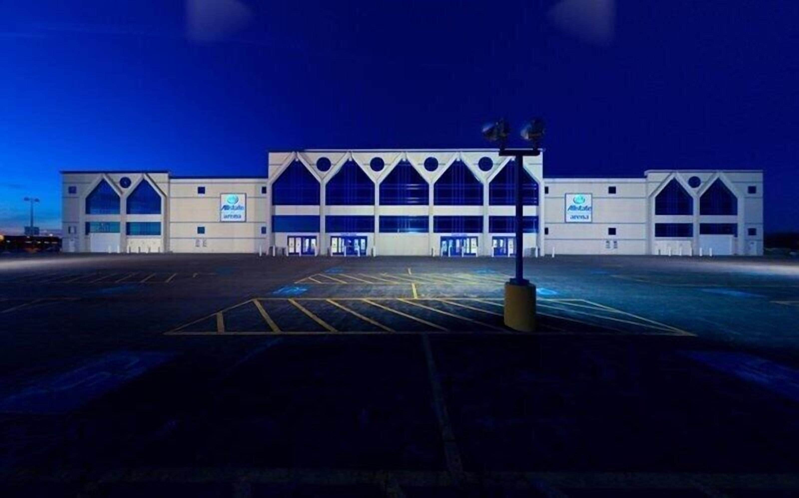 Un ampio edificio moderno con una facciata simmetrica, diversi accessi e un parcheggio di fronte.