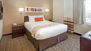 A hotel room with a large bed, a nightstand, a wall-mounted phone, and a painting above the bed. - MainStay Suites Northbrook Wheeling (Wheeling)