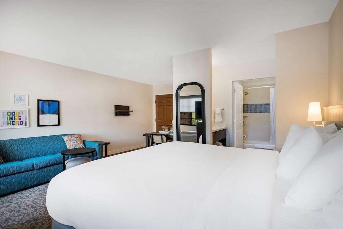 Een hotelkamer met een groot bed, een blauwe bank, een klein tafeltje, een spiegel en een deur naar een badkamer.