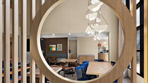 Un interior moderno con un marco de madera circular, mesas y sillas de madera, y un área de cocina visible a través del marco.