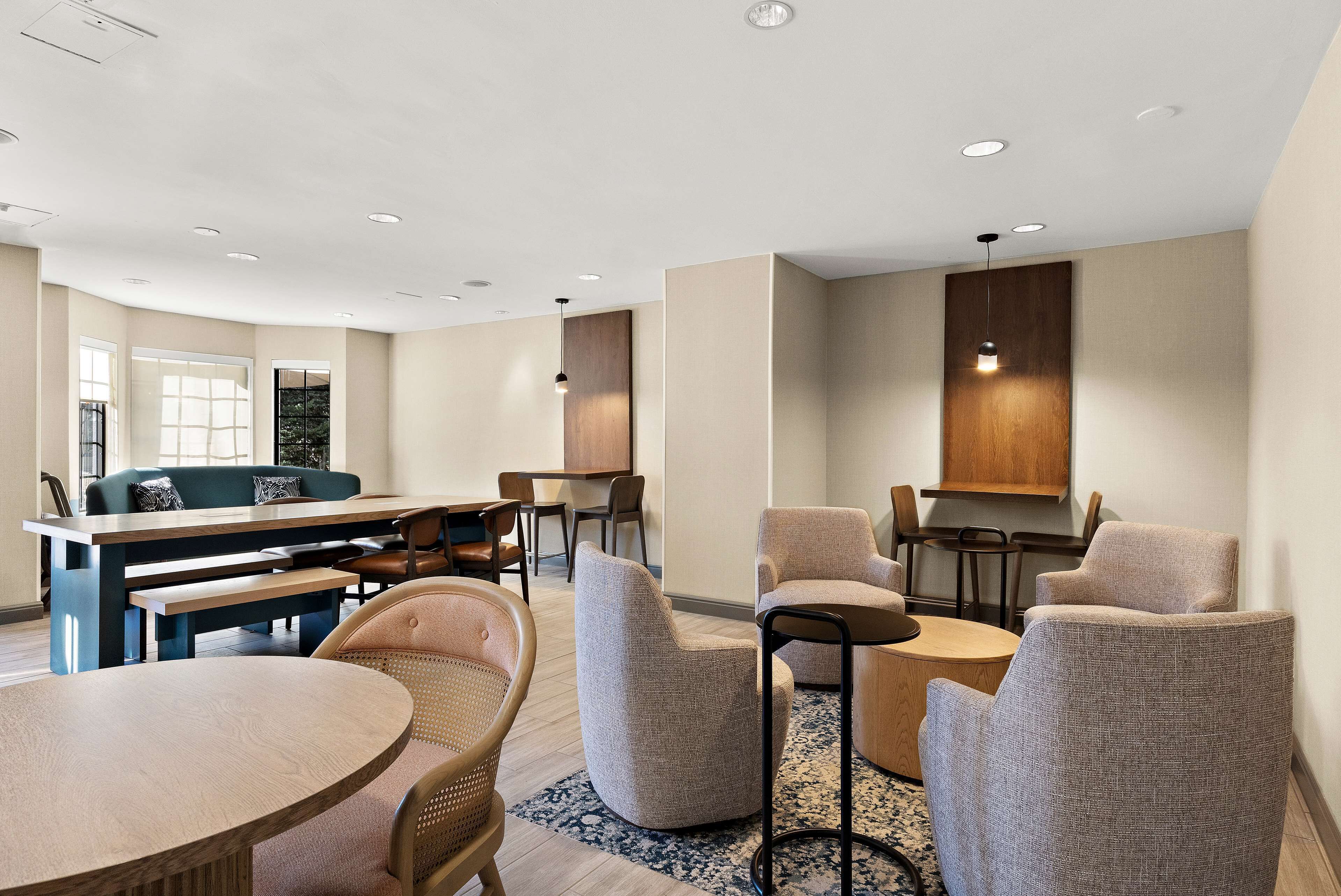 Un hall d’hôtel moderne avec une table de salle à manger ronde, plusieurs fauteuils, un canapé et un coin bar.