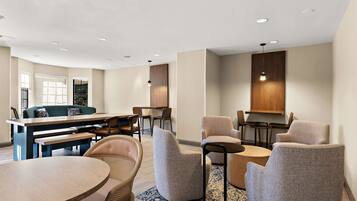 A modern hotel lobby with a round dining table, several armchairs, a sofa, and a bar area.