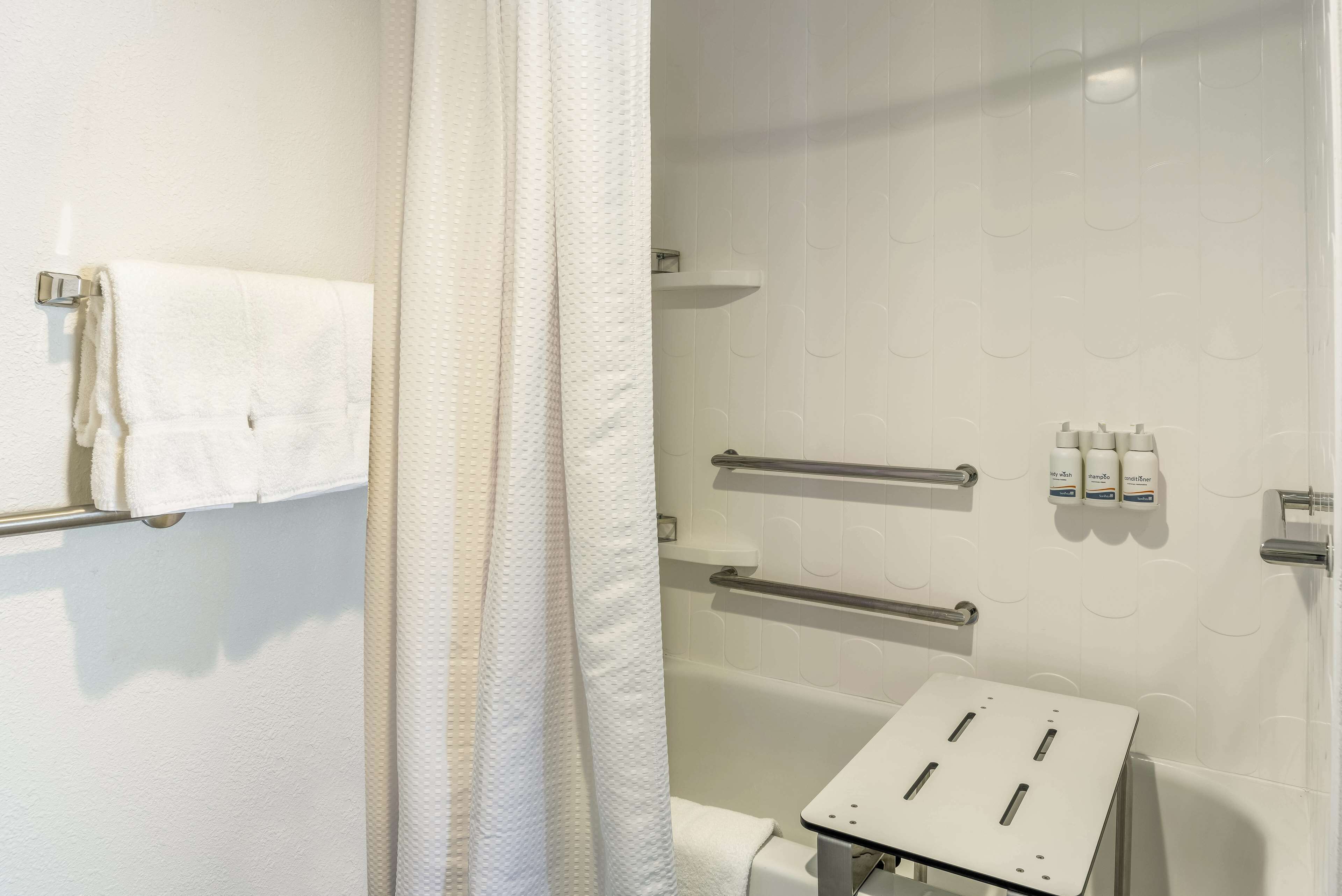 Une salle de bain équipée d’une baignoire, d’un porte-serviettes, de barres d’appui et d’une petite table avec des prises électriques.