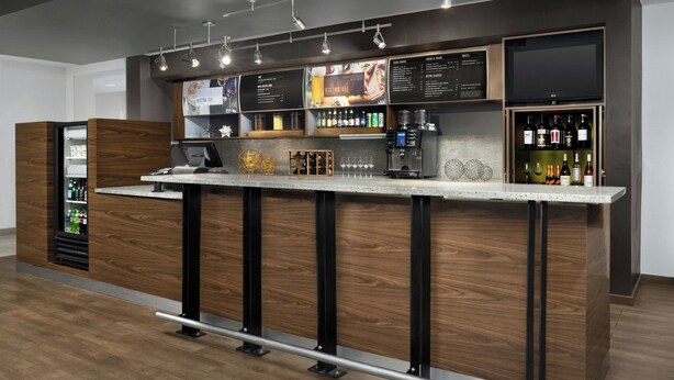 A modern bar area with a wooden counter, a menu board, and a wine display. - Courtyard by Marriott Lakeland (Lakeland)