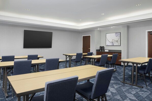 A conference room with multiple tables and chairs, a large screen, and a coffee station.