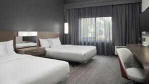 A hotel room with two beds, a desk, a chair, a lamp, and a large window with curtains. - Courtyard by Marriott Lakeland (Lakeland)