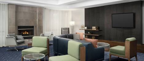 A modern hotel room with a fireplace, comfortable seating, a flat-screen TV, and a large window.