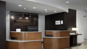 A reception area with two wooden reception desks, a wall-mounted information board, and a sign indicating the name of the hotel. - Courtyard by Marriott Lakeland (Lakeland)