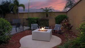 An outdoor patio with a square fire pit table, surrounded by chairs, under a sunset sky. - Courtyard by Marriott Lakeland (Lakeland)