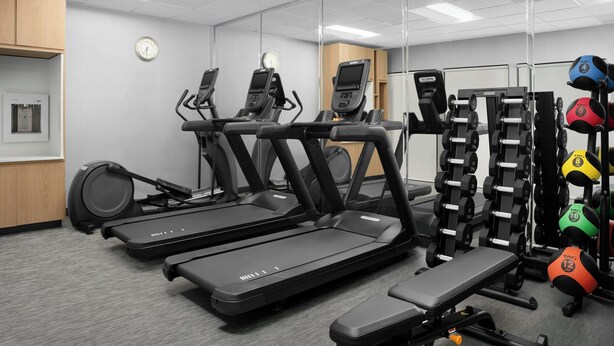 Une salle de sport équipée de tapis de course, d’appareils de musculation et de différents ballons d’exercice.