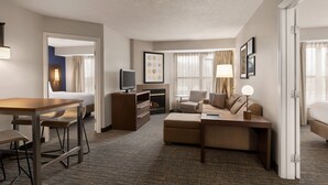 Ein Hotelzimmer mit einer Sitzecke, einem Esstisch mit Stühlen, einem Fernseher und einem Kamin.