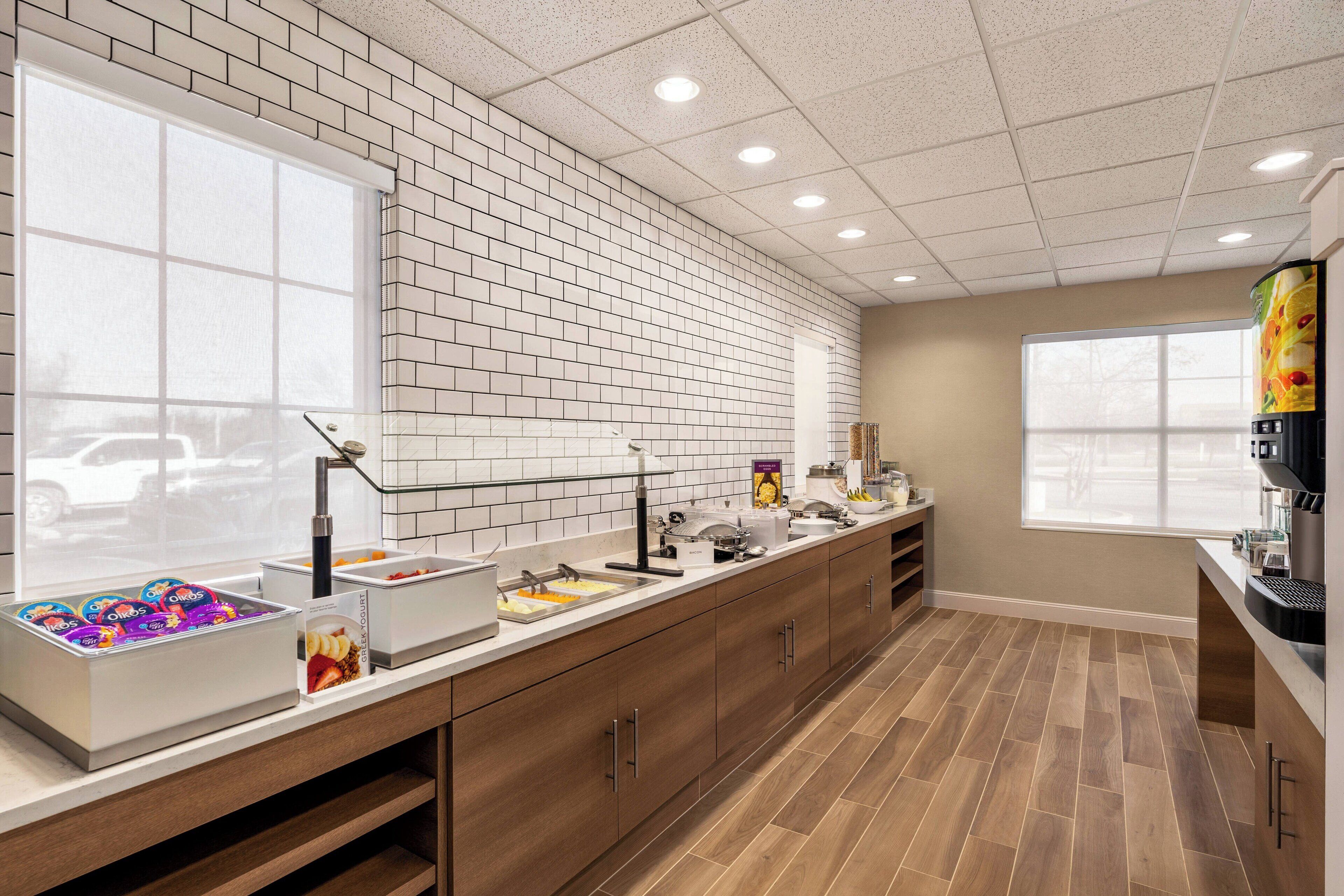 A modern kitchen with a brick backsplash, wooden cabinets, and a large window providing natural light.