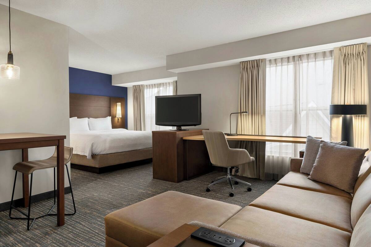 Habitación de hotel con cama, escritorio con televisor, sofá, sillón y una mesita.