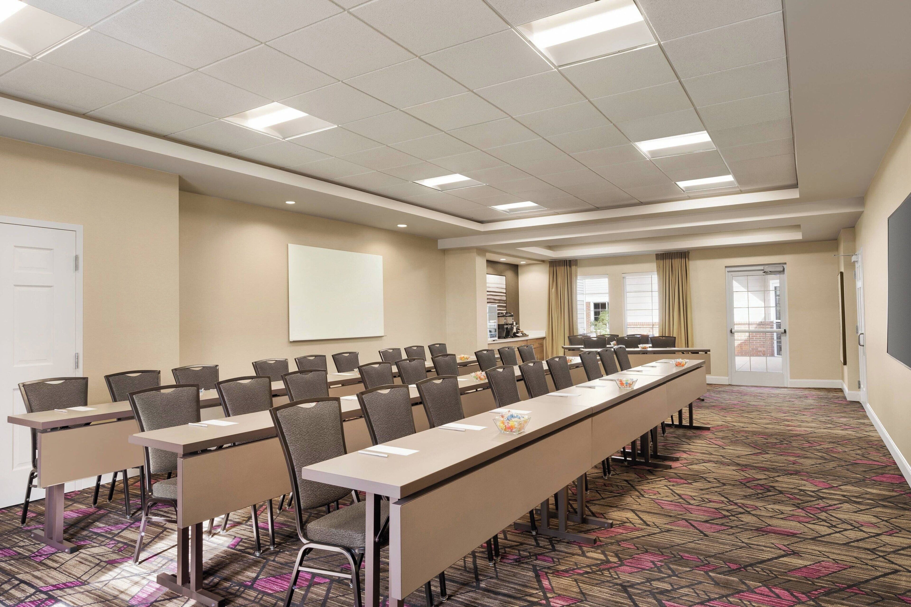 A conference room with long tables, chairs, a projector screen, and a patterned carpet.