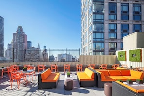 Une terrasse sur le toit avec des sièges extérieurs, une vue panoramique sur la ville et un bâtiment à l’architecture moderne.