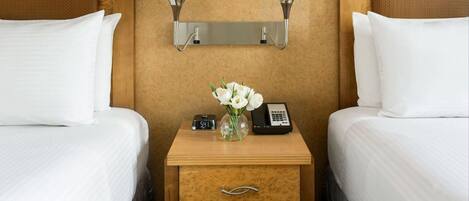 A hotel room with two beds, a nightstand with a clock and phone, and wall-mounted lamps.