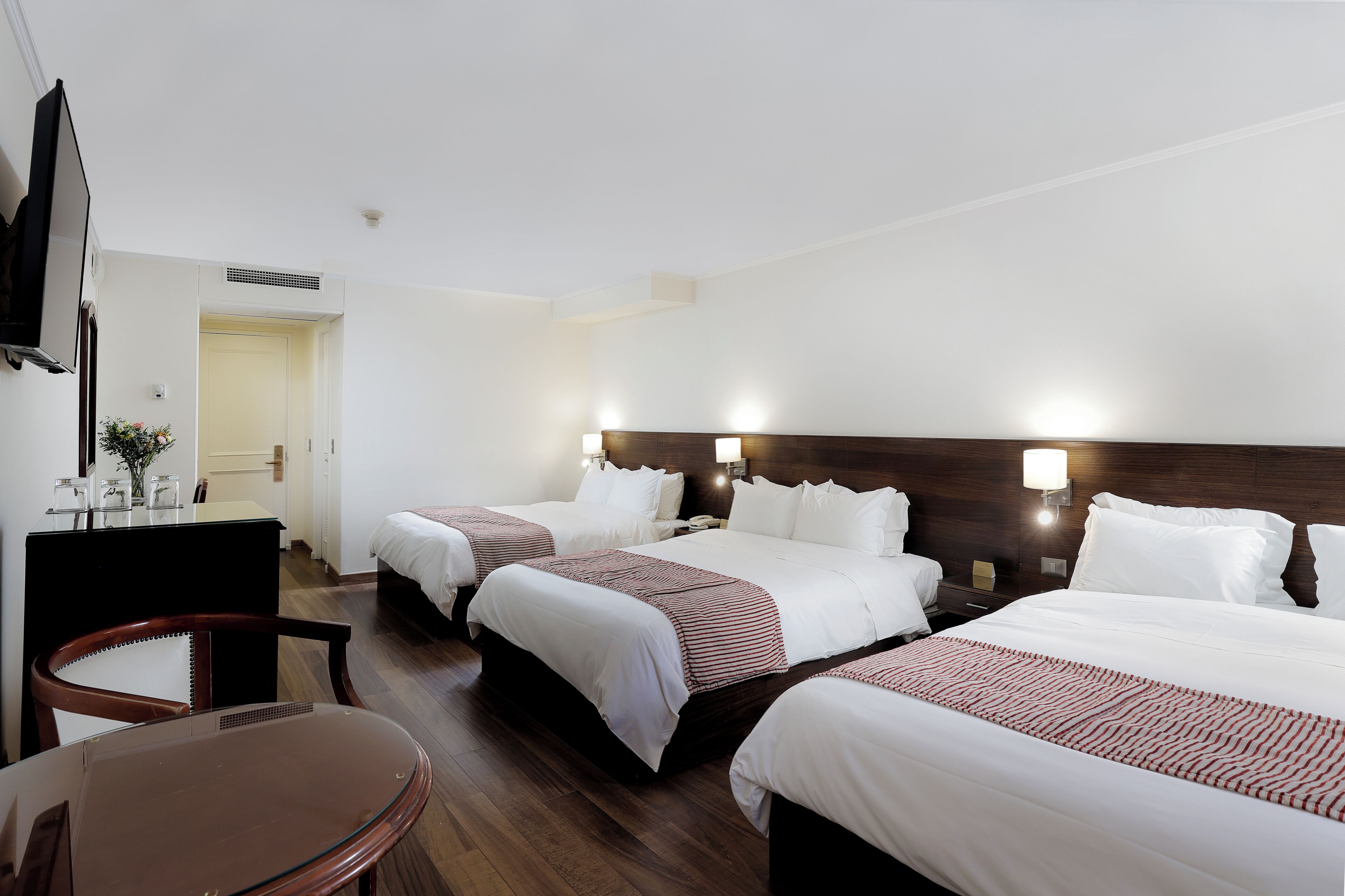 Une chambre d’hôtel avec trois lits, un bureau, une chaise et un téléviseur.