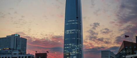 A cityscape with a prominent skyscraper, a modern building with a sign, and surrounding urban structures.