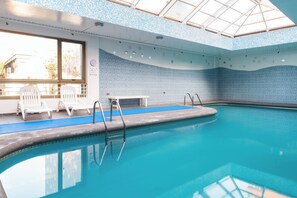 An indoor swimming pool with clear blue water, white lounge chairs, and a skylight ceiling. - MR Hotel (Santiago)