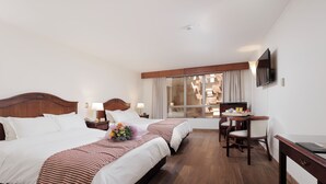 Habitación de hotel con dos camas, un escritorio, una silla, un televisor y una ventana con cortinas.