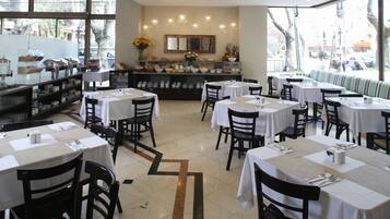 A restaurant with multiple tables and chairs, a buffet area, and large windows offering a view of the street.
