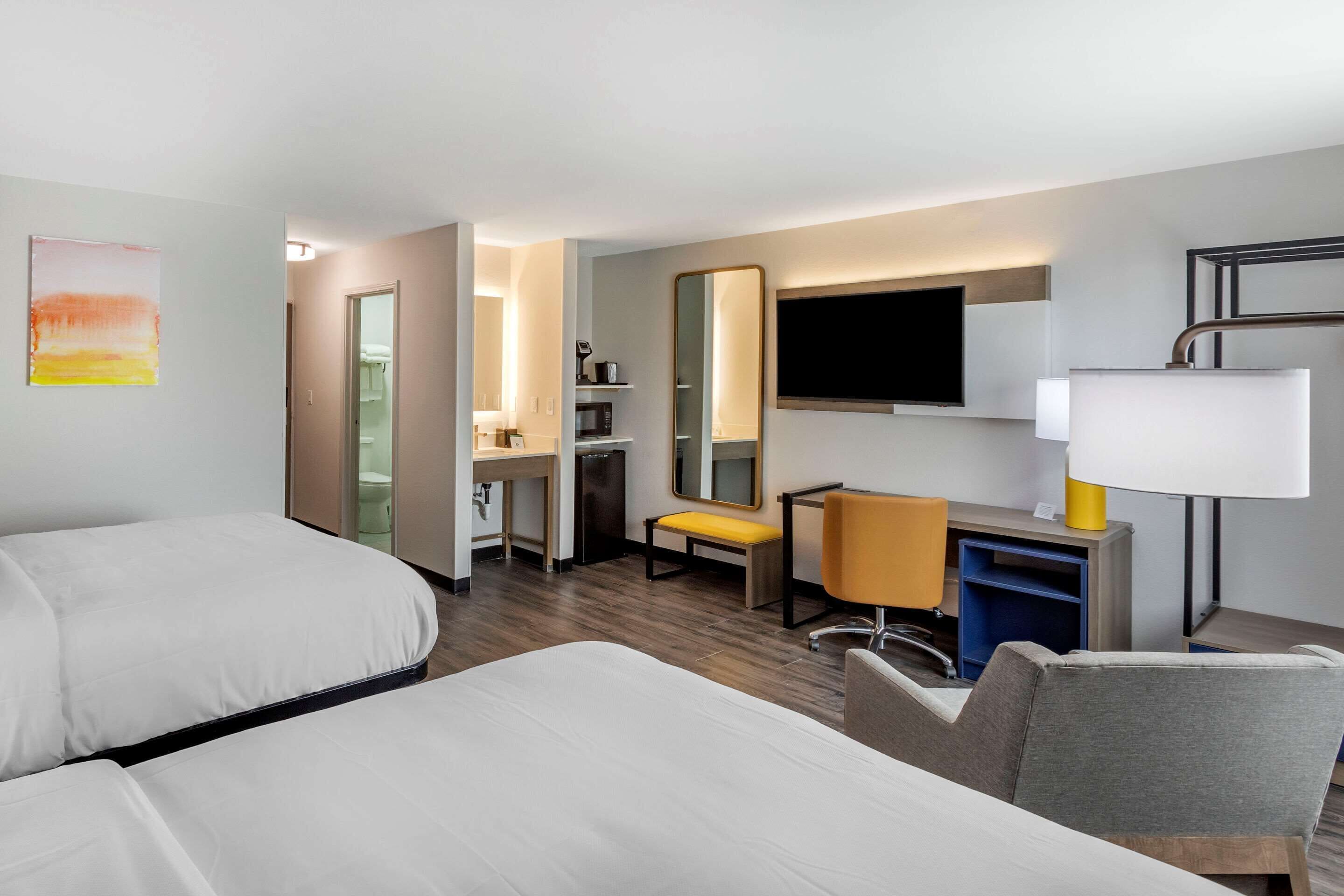 A hotel room with two beds, a desk, a chair, a TV, and a mirror.