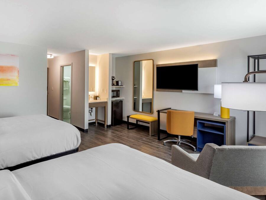 A hotel room with two beds, a desk, a chair, a TV, and a mirror.