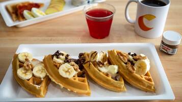 A plate of waffles topped with bananas and nuts, a cup of red beverage, and a mug of coffee on a wooden table.
