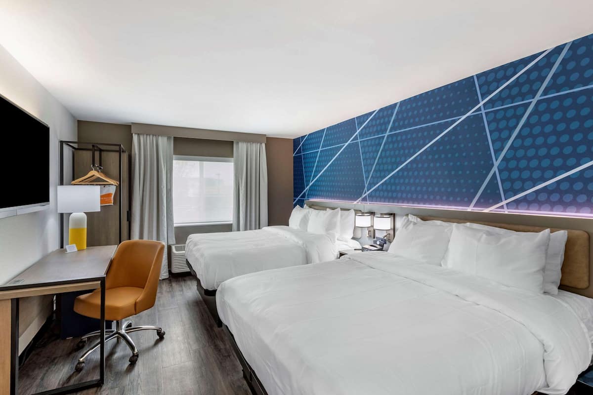Une chambre d’hôtel avec deux lits, un bureau avec une chaise, une télévision et une fenêtre avec des rideaux.