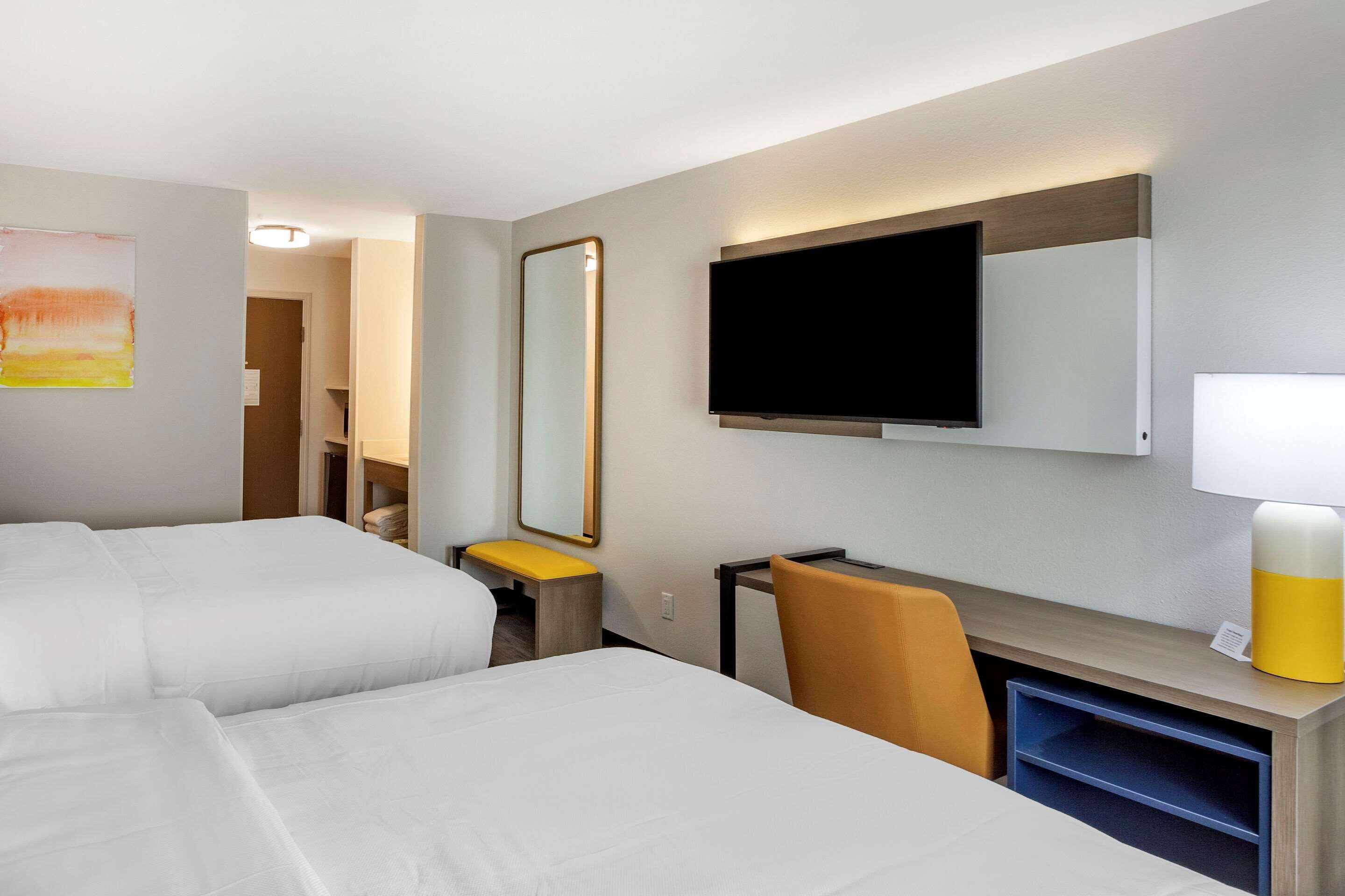 Habitación de hotel con dos camas, un escritorio, una silla, un televisor, un espejo y una lámpara.