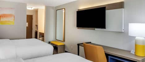 Habitación de hotel con dos camas, un escritorio, una silla, un televisor, un espejo y una lámpara.