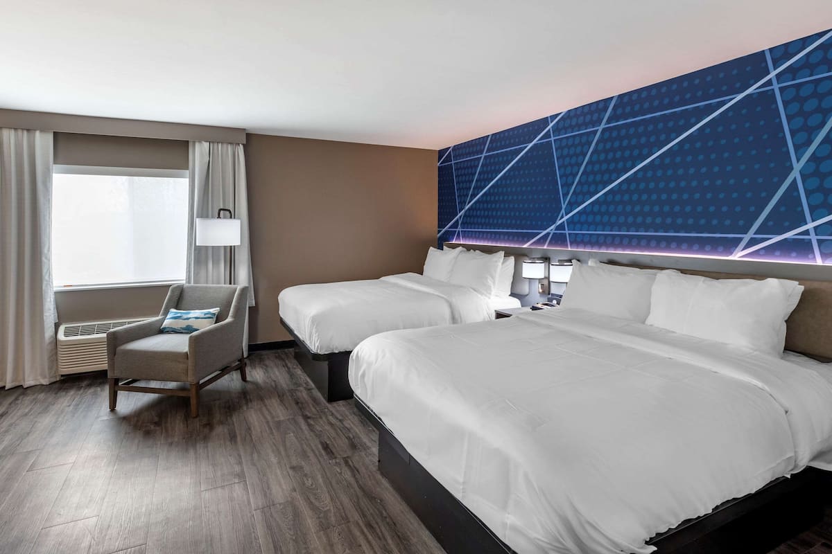 Une chambre d’hôtel avec deux lits, une chaise, une lampe et un grand mur orné d’un motif géométrique.