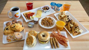 A breakfast spread on a wooden table with various pastries, sandwiches, and beverages.