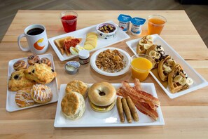 A breakfast spread on a wooden table with various pastries, sandwiches, and beverages.