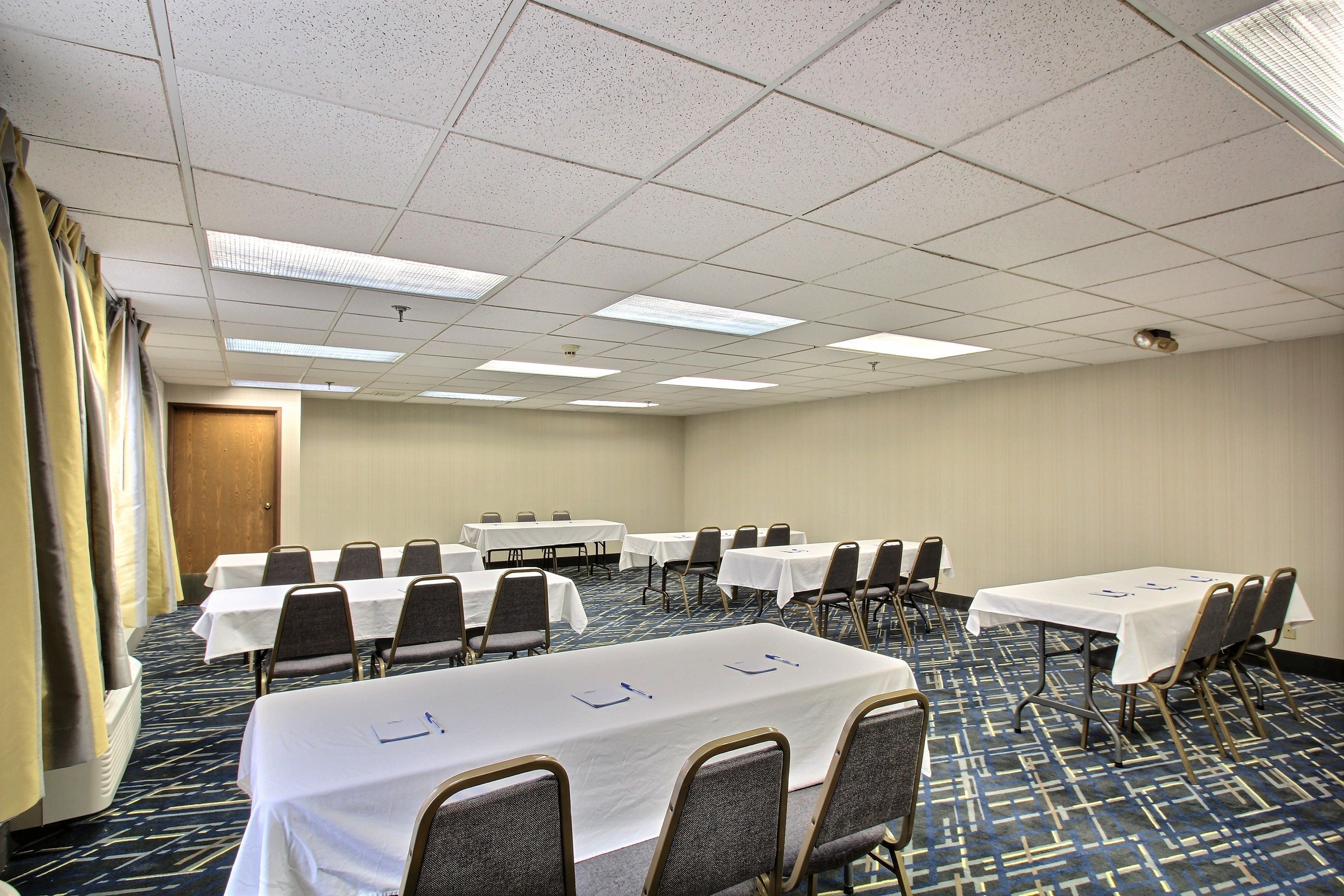 A conference room with multiple tables and chairs, a carpeted floor, and a ceiling with fluorescent lights.