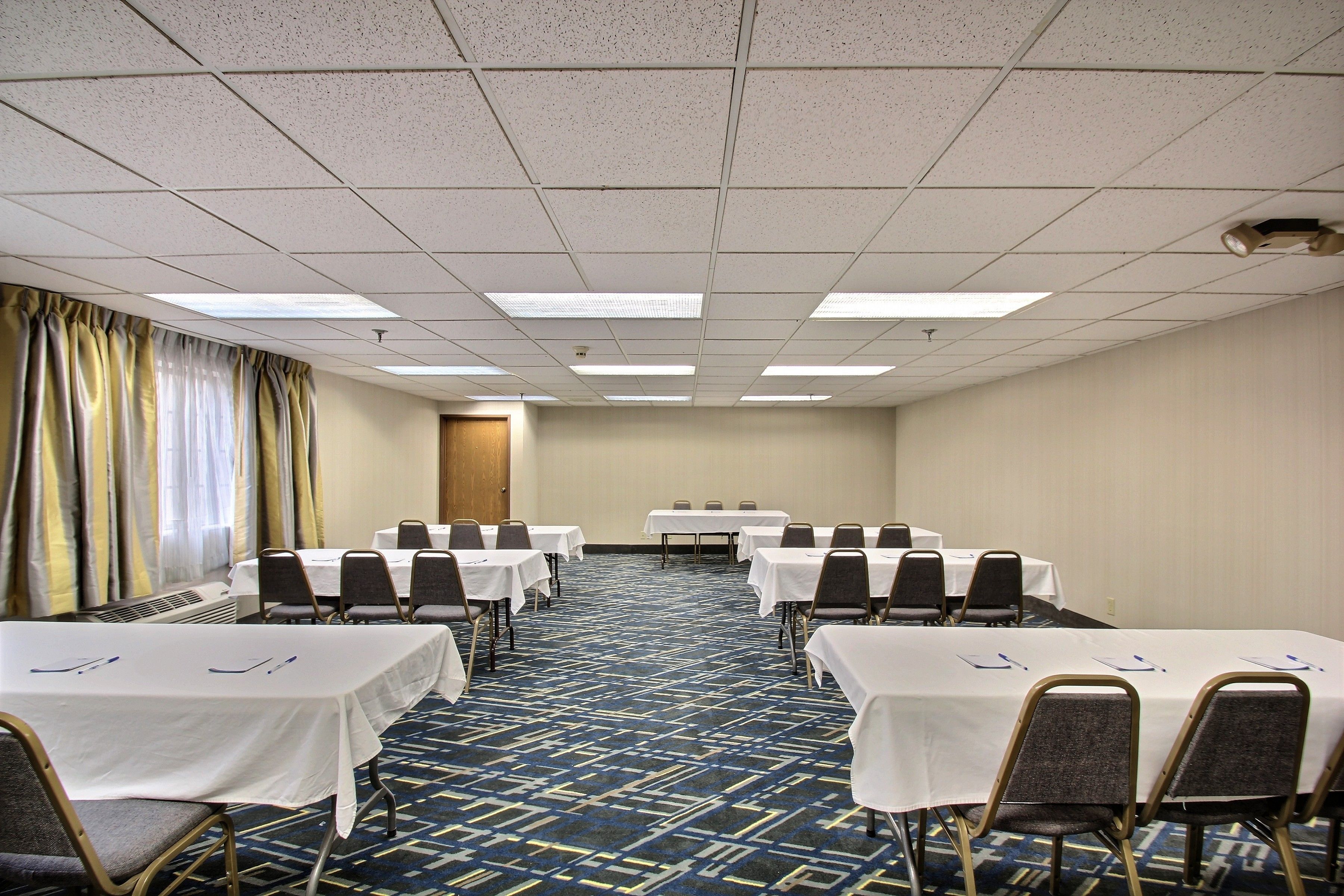 A conference room with tables and chairs, a patterned carpet, and a plain ceiling.